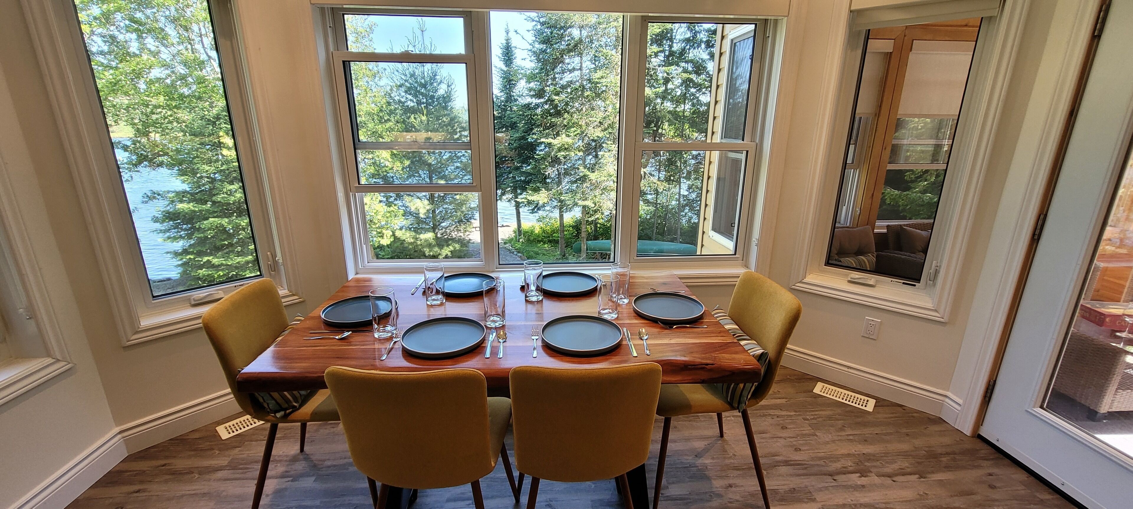 A dining area with a table set for six, large windows, and a view of trees and water.