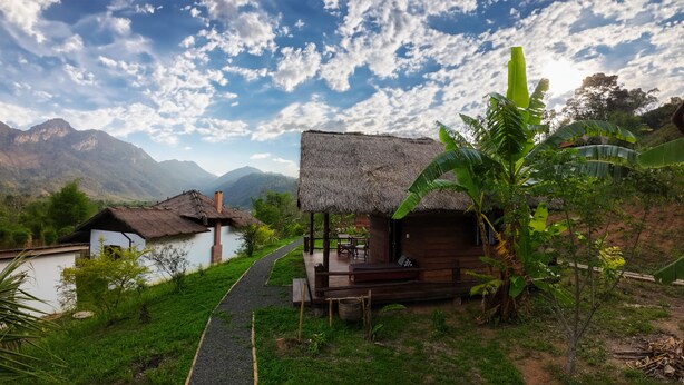 A rural setting with thatched-roof huts, a paved path, and lush greenery. - Naga Lodge (Luang Prabang)