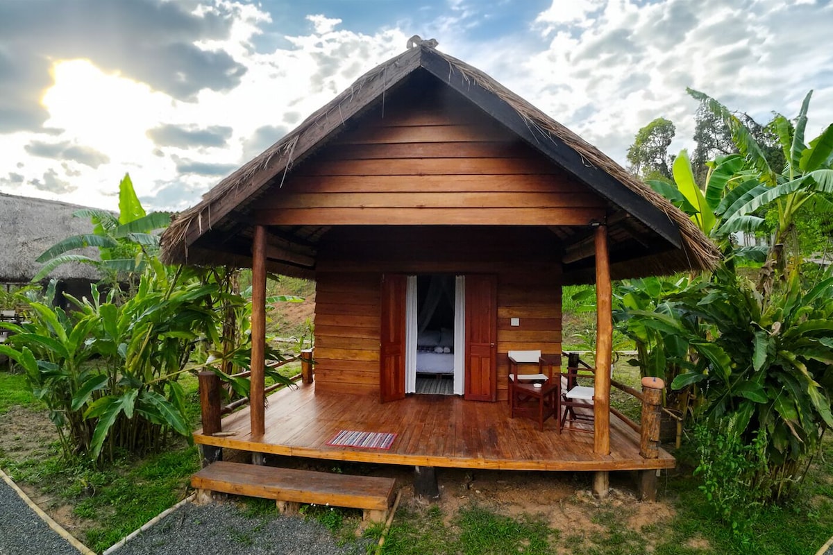 A wooden cabin with a porch, a bed, and a table.