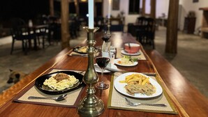 A long wooden table with plates of food, a candle, and a wine glass. - Naga Lodge (Luang Prabang)