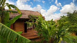 A wooden hut with a thatched roof surrounded by lush greenery. - Naga Lodge (Luang Prabang)