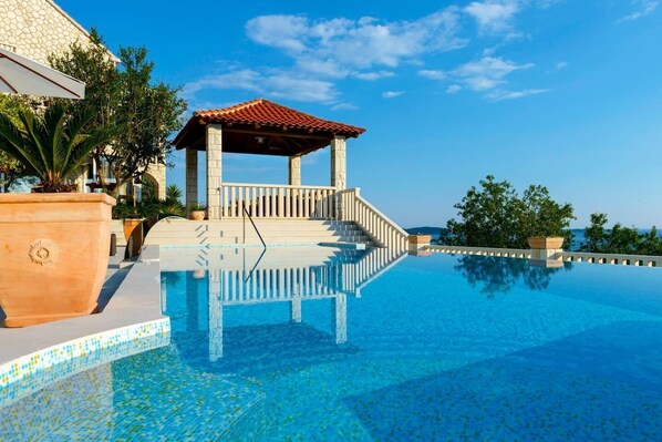 Una piscina infinita con un pabellón, cielo azul despejado y vista al mar.