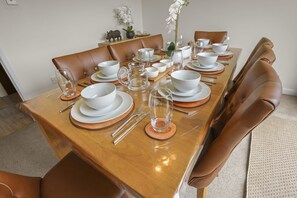 A dining table set with white plates, bowls, and cutlery, surrounded by brown leather chairs. - House -  Sleeps 6 & Free parking (Great Yarmouth)