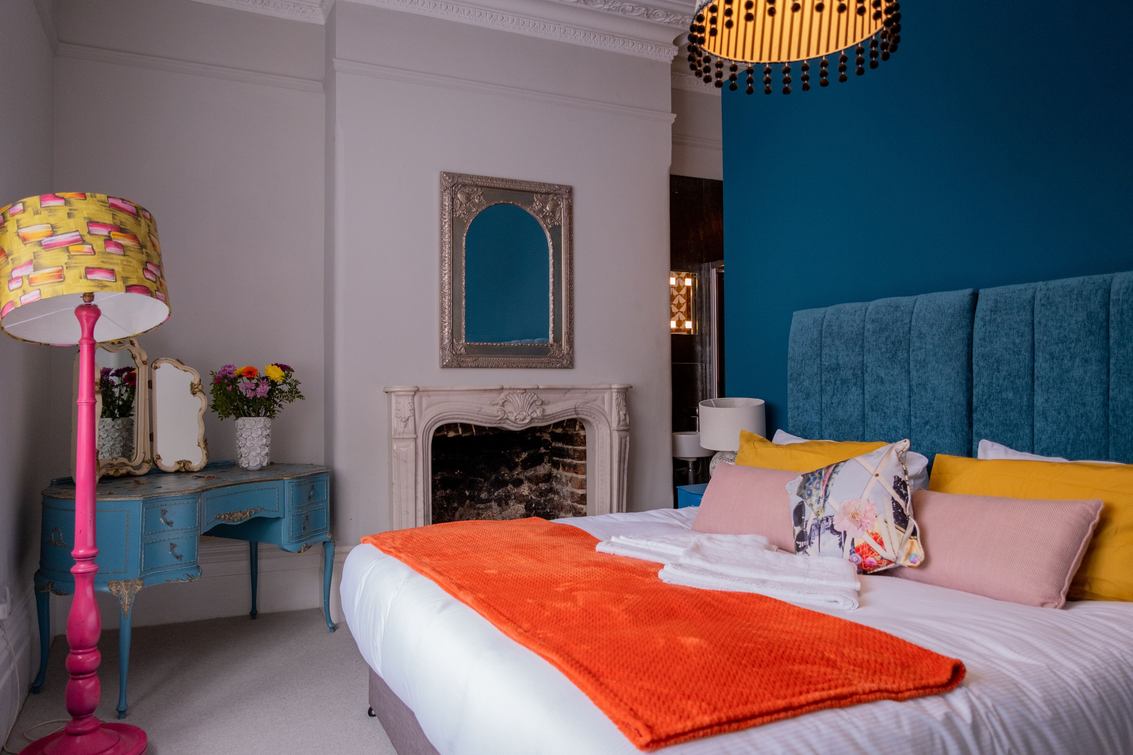 A bedroom with a bed, a dresser, a mirror, a fireplace, and a hanging light fixture.