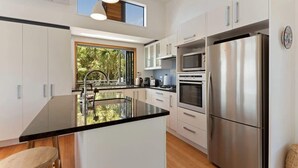 Uma cozinha moderna com armários brancos, uma geladeira de aço inoxidável e uma ilha grande com bancada preta.