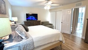 Une chambre à coucher avec un lit, un téléviseur posé sur une commode, un ventilateur de plafond et une porte-fenêtre coulissante donnant sur un balcon.