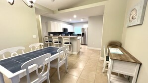 Un coin repas avec une table et des chaises, une cuisine en arrière-plan et une petite table en bois sur laquelle est posé un menu.
