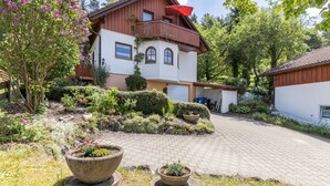 Una casa de dos pisos con un balcón, rodeada por un jardín con diversas plantas y flores.