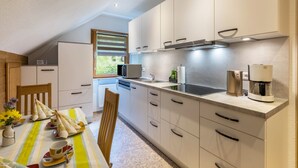 Una cocina moderna con armarios blancos, un microondas, una cafetera y un comedor con mantel a rayas y sillas.