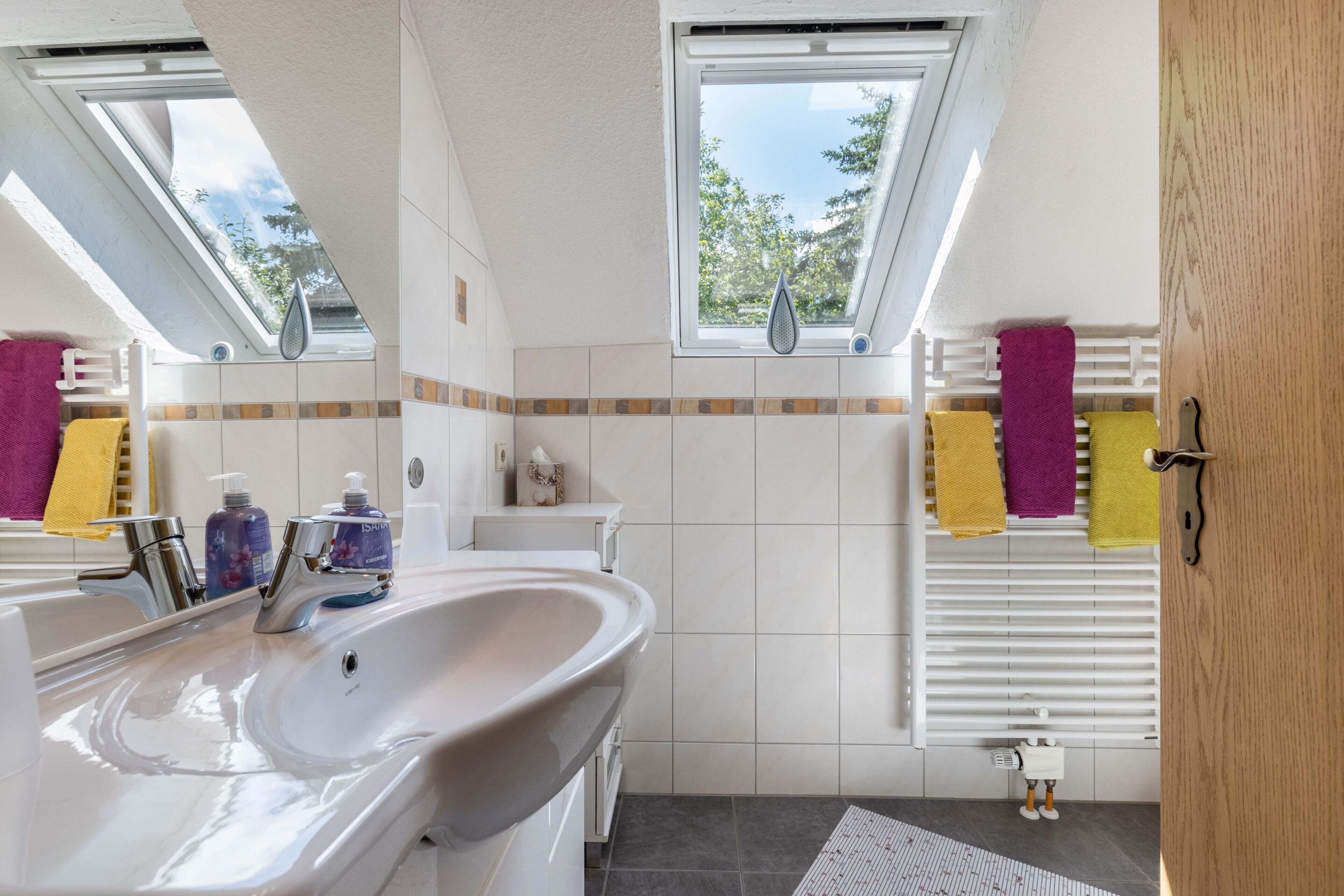 Ein modernes Badezimmer mit Oberlicht, weißen Fliesen, einem großen Waschbecken und einem Handtuchhalter.