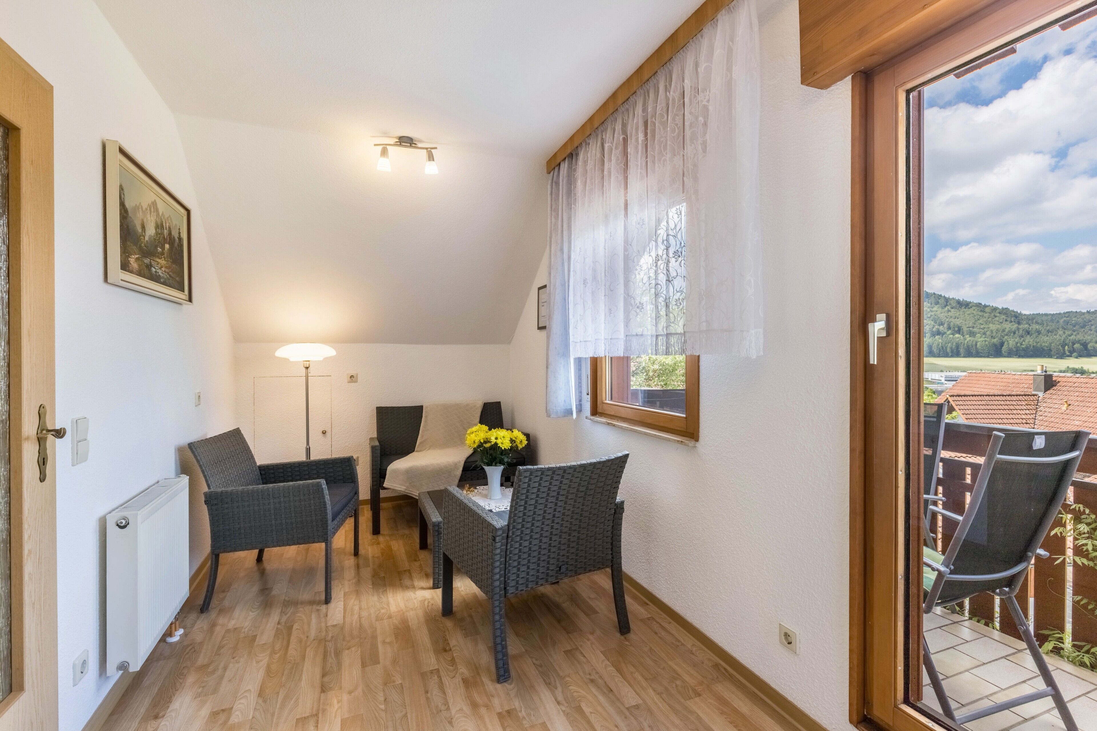 Una habitación pequeña con una mesa, dos sillas, una lámpara y una ventana con vistas a un jardín.