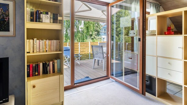Une pièce dotée d’une porte-fenêtre coulissante donnant sur une terrasse extérieure, d’une bibliothèque, d’un téléviseur et d’un meuble.