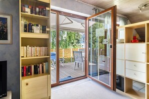 Une pièce dotée d’une porte-fenêtre coulissante donnant sur une terrasse extérieure, d’une bibliothèque, d’un téléviseur et d’un meuble.