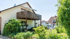 Une maison avec un balcon, un jardin où poussent différentes plantes, et un camping-car garé au fond.