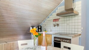 Une cuisine avec un plafond en bois, un mur recouvert de carreaux, une cuisinière et une table à manger agrémentée d’une bouteille de vin et de verres.