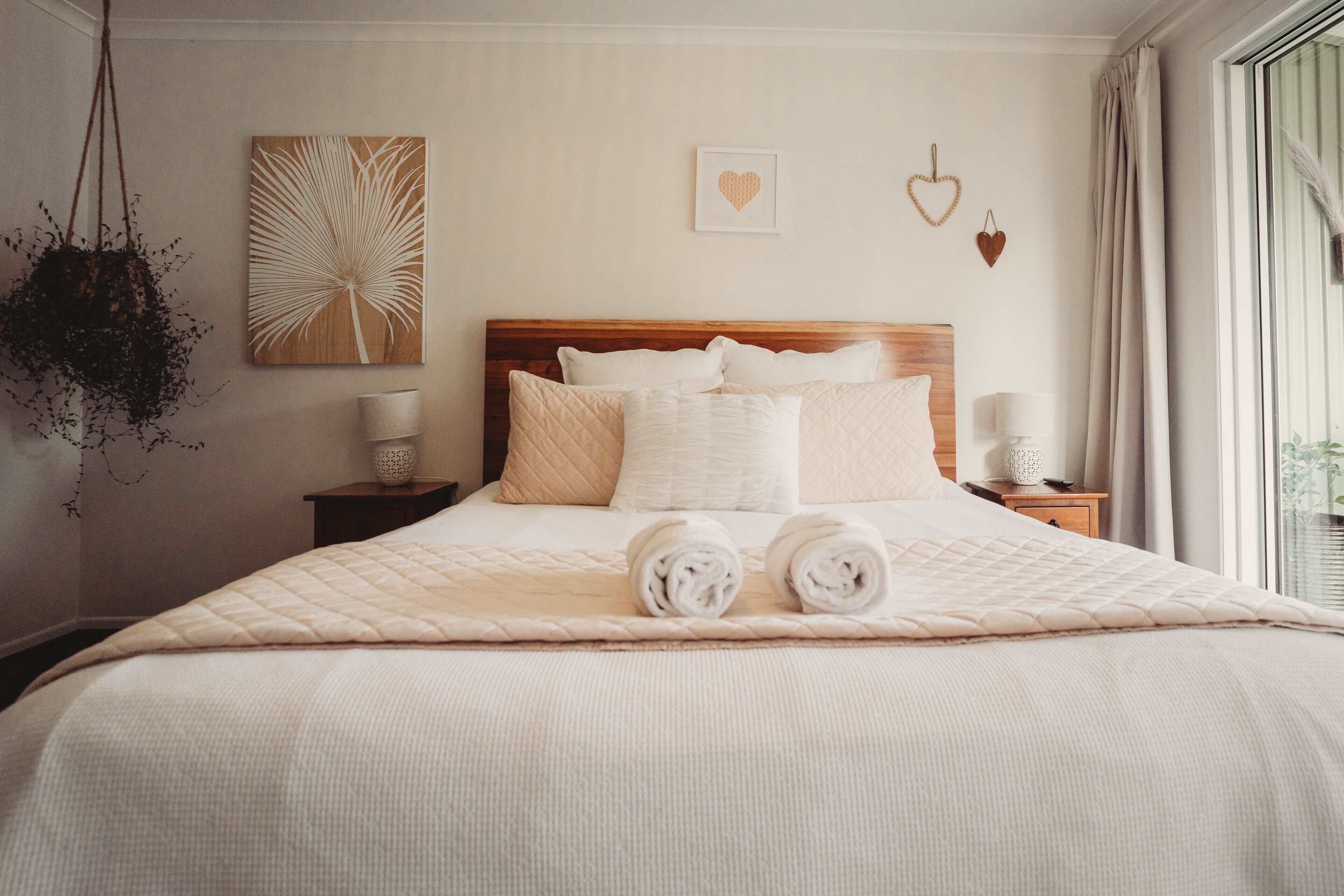 A neatly made bed with a quilted bedspread, two rolled towels, and a wooden headboard.