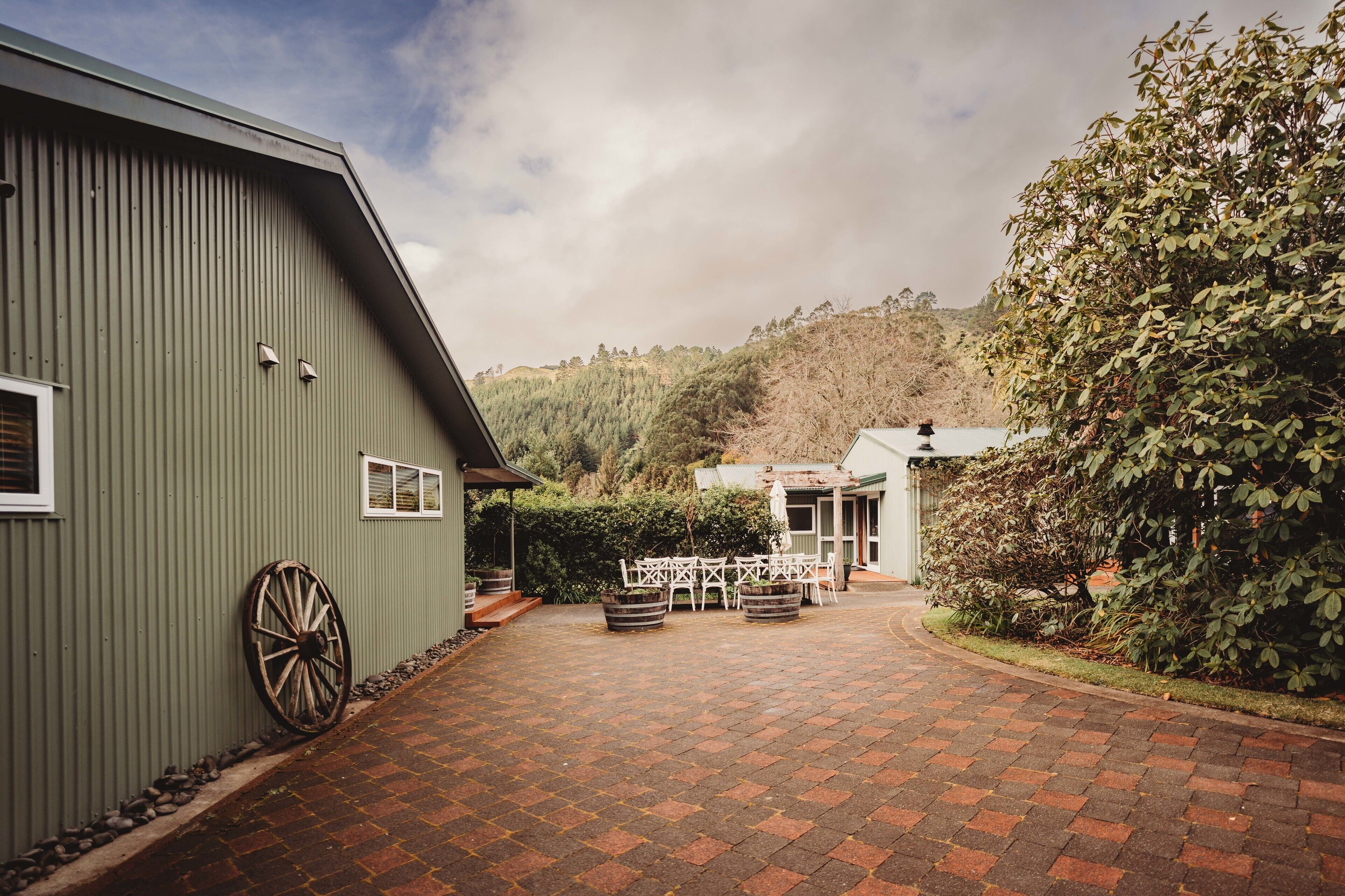 A courtyard with a paved walkway, a large wheel, and outdoor furniture.