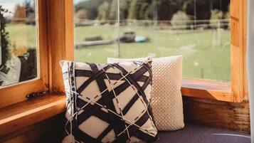 A window seat with two cushions, a view of a green field, and a wooden window frame.