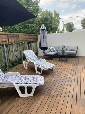 Eine Holzterrasse mit zwei Liegestühlen und einem kleinen Tisch mit einem Blumentopf.