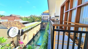 A courtyard with a pool, a sign, and a view of neighboring buildings. - Kamandaka Living (Kuta)