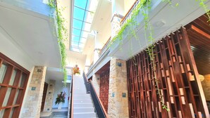 A multi-level interior with a central staircase, stone walls, and hanging plants. - Kamandaka Living (Kuta)
