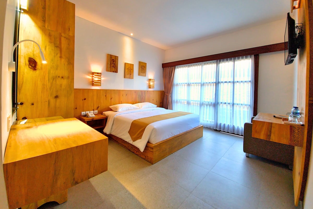 A hotel room with a wooden headboard, a large bed, a desk, and a television.