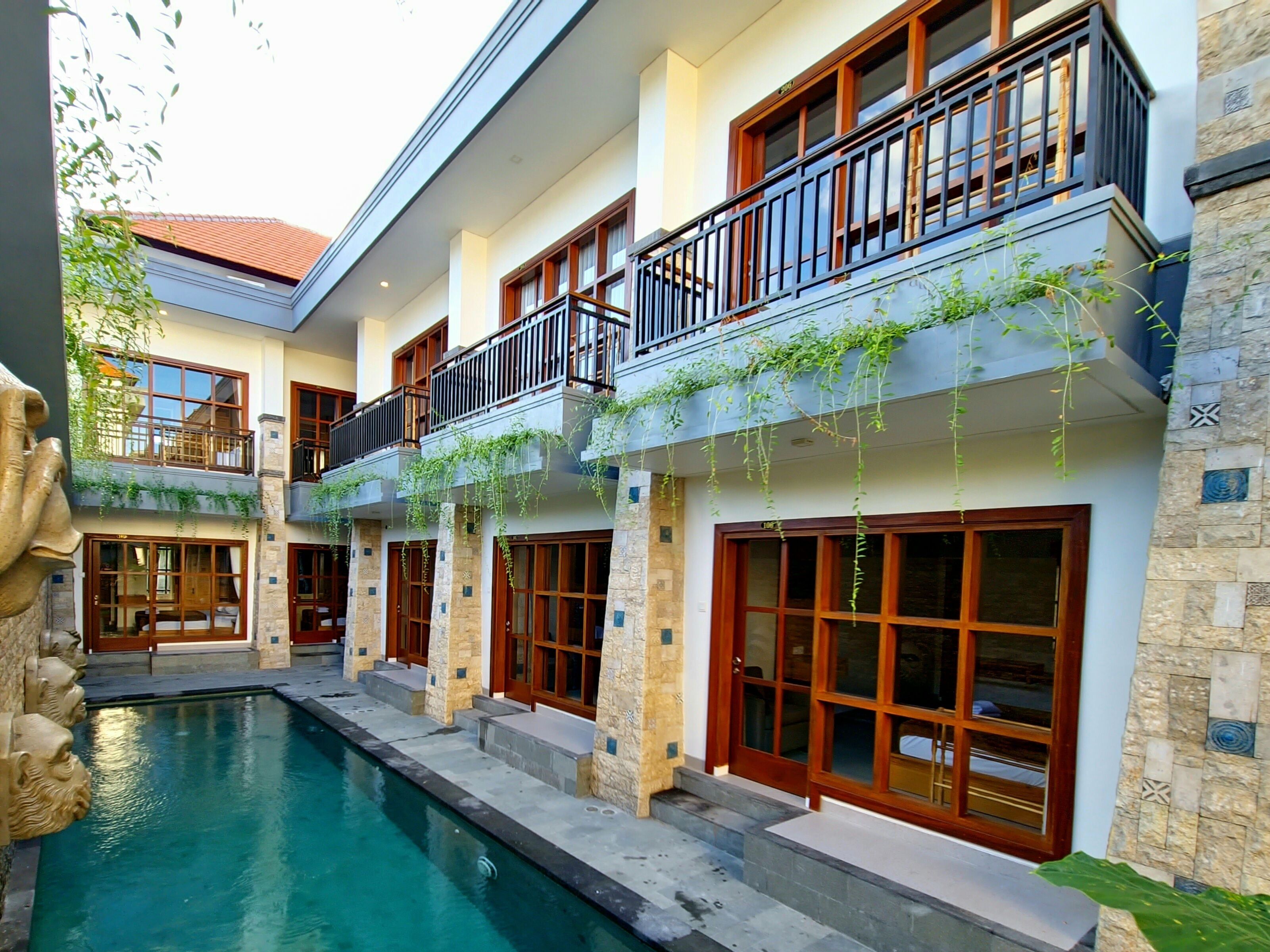 A multi-story building with a swimming pool, stone walls, and balconies with wooden railings.