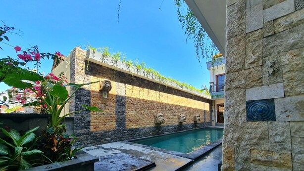 A pool area with stone walls and a clear blue sky. - Kamandaka Living (Kuta)