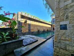 A pool area with stone walls and a clear blue sky. - Kamandaka Living (Kuta)