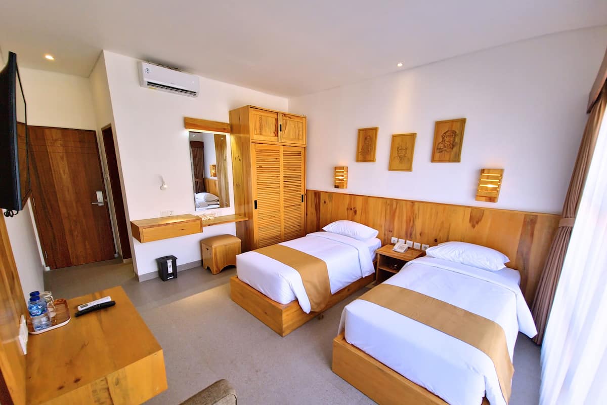 A hotel room with two beds, a wooden desk, a mirror, and a wardrobe.