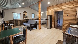 Ein gemütliches Blockhausszimmer mit Essbereich, einer Couch, einem Bett, einem Kühlschrank und einer Holzwand.