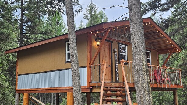 Eine Hütte mit Holzfassade, einer Veranda mit Lichterketten und einer Holztreppe, die zum Eingang führt.