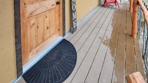 Eine Holzhütte mit einer großen Holztür, einem Willkommensschild, einem Fenster und einem roten Stuhl auf der Veranda.