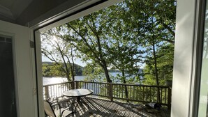 Une terrasse en bois avec une table et des chaises, donnant sur un lac, avec des arbres et des collines en arrière-plan.