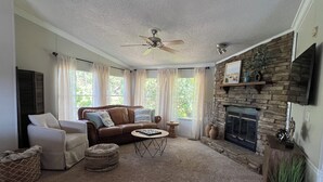 Un salon chaleureux avec une cheminée, un canapé en cuir, une table basse et un ventilateur de plafond.