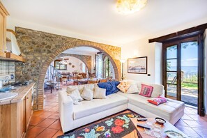 A cozy living room with a stone archway, a white sofa, a kitchen area, and a view of the outdoors. - Beautiful Casolare With Pool Among Green, Ficulle, Italy (Ficulle)