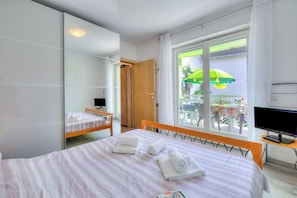 Quarto de hotel com cama, escrivaninha, televisão e janela com vista para o exterior.
