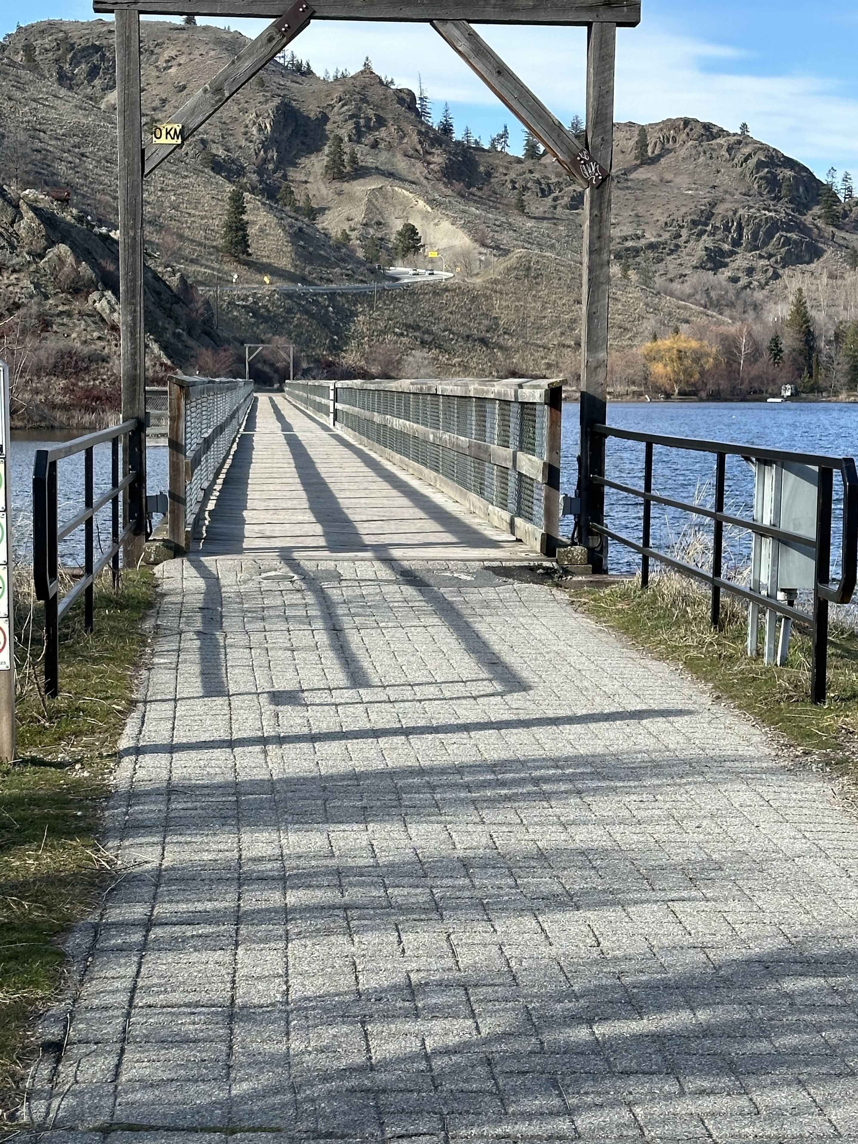 Un pont piétonnier enjambant une rivière, avec une colline rocheuse en arrière-plan.