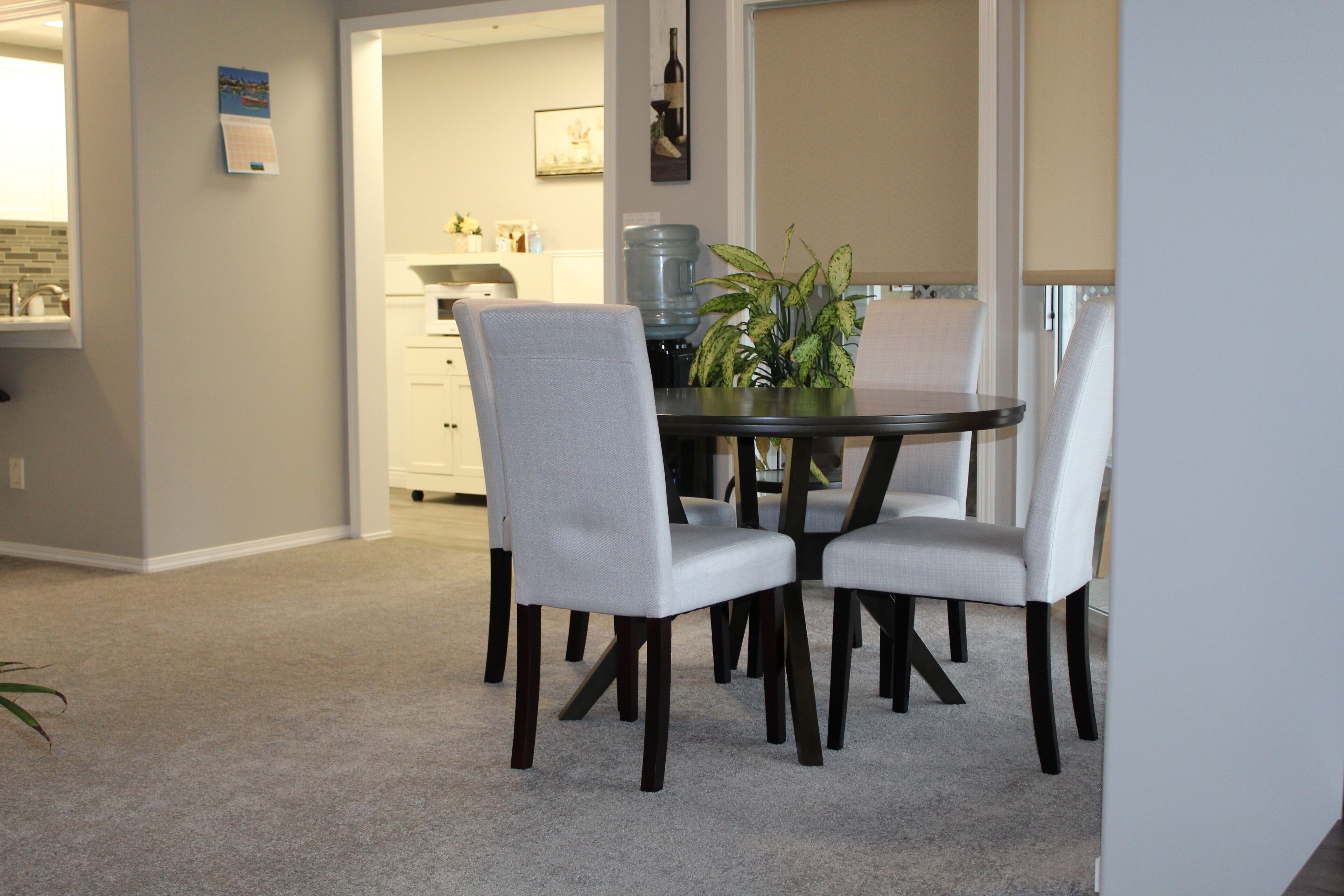 A dining area with a round table and four chairs, a water dispenser, and a potted plant.