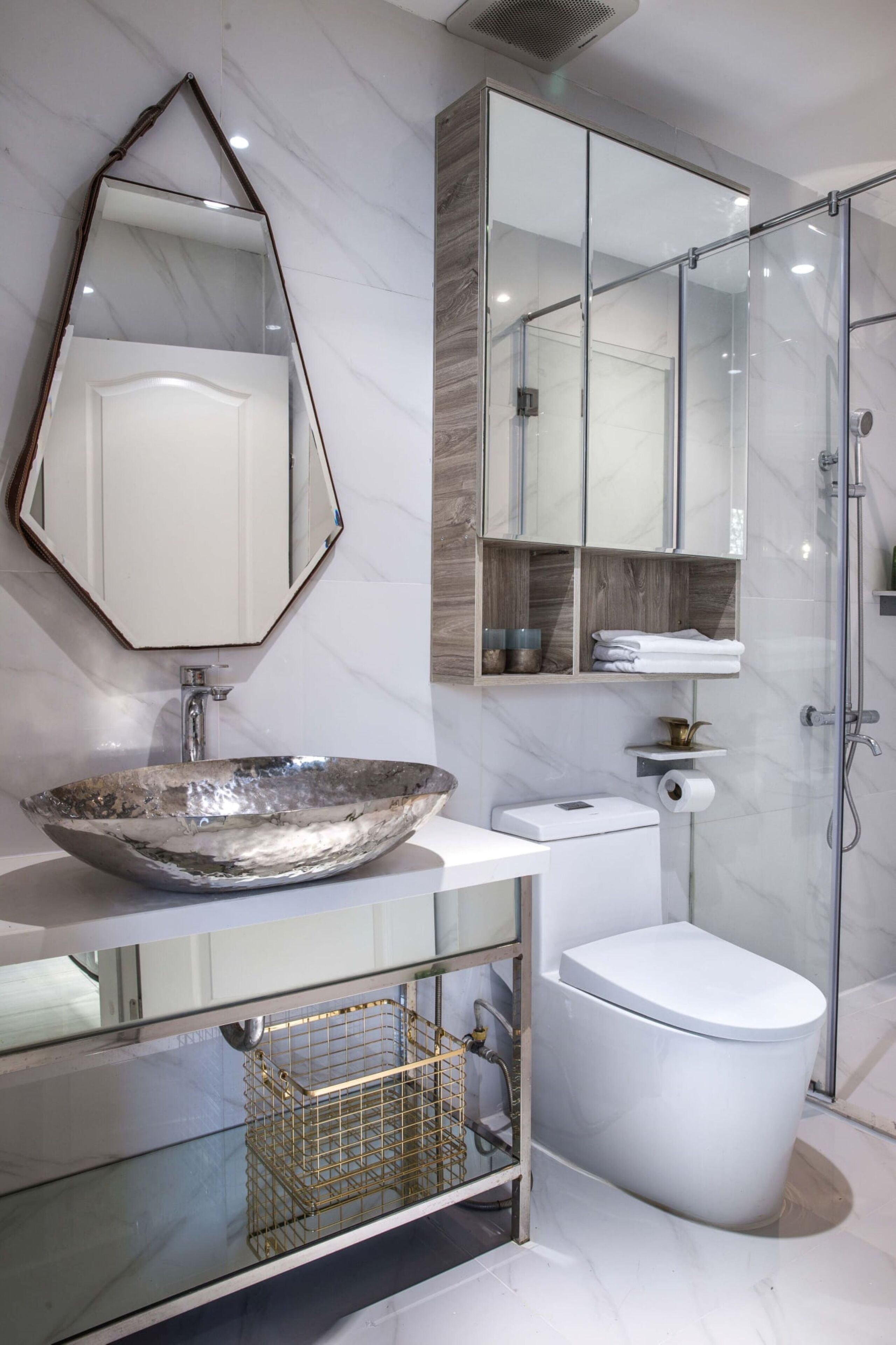 Une salle de bain moderne dotée d’un grand lavabo ovale, de toilettes sur pied, d’une douche à parois de verre et d’un meuble-lavabo avec miroir et étagères intégrées.