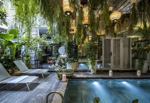 Een rustig binnenzwembad met ligbedden, hangplanten en sfeerverlichting.