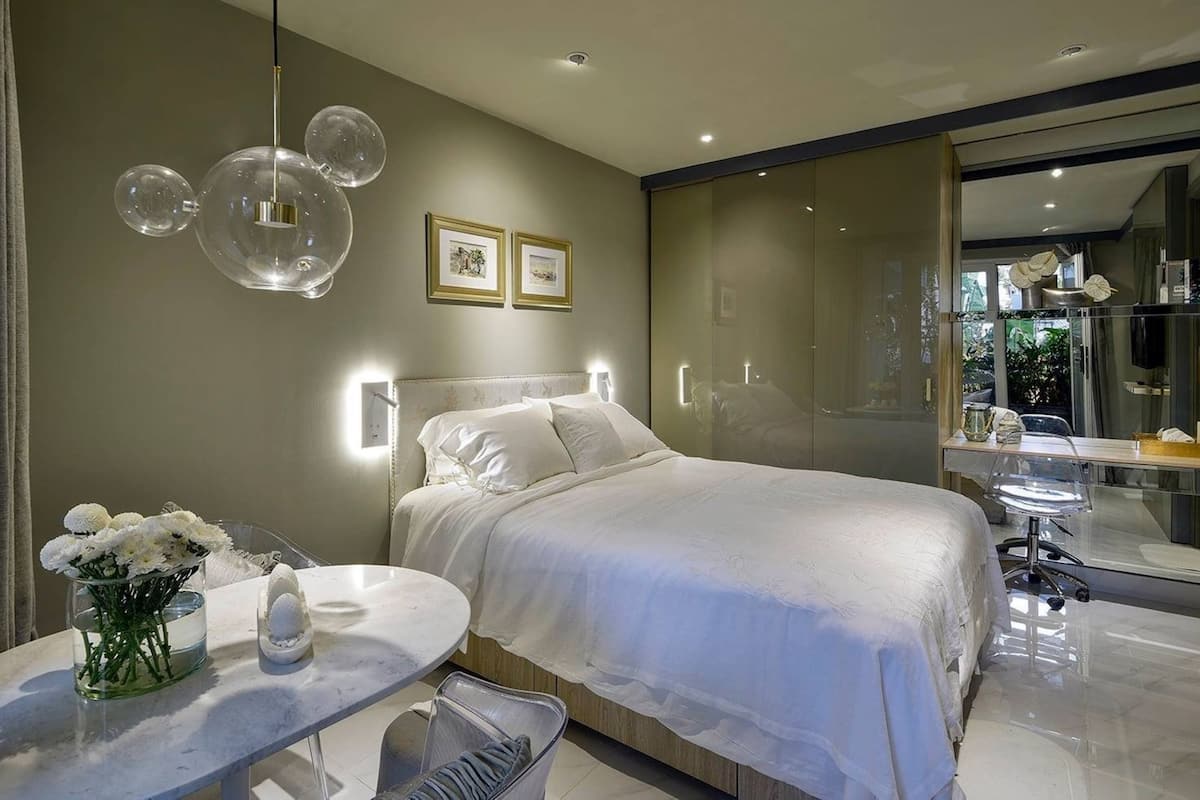 Quarto moderno com uma cama grande, mesas de cabeceira, box de chuveiro em vidro e vista para o exterior.