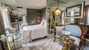 A modern hotel room with a glass partition, a bed, a seating area with a blue sofa, a glass table, and a decorative lamp. - Bed In Town Saigon (Ho Chi Minh City)
