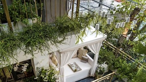 A high-ceilinged indoor garden with a white cushioned seating area, surrounded by lush greenery and potted plants. - Bed In Town Saigon (Ho Chi Minh City)