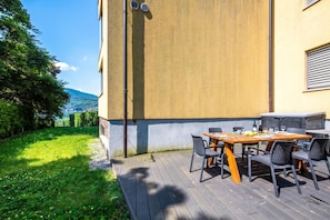 Une terrasse avec une table et des chaises en bois, un barbecue et une vue sur un lac et des montagnes.