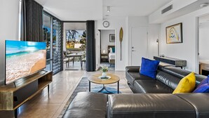 Una sala de estar moderna con un televisor grande, un sofá de cuero y un comedor con vista a la playa.