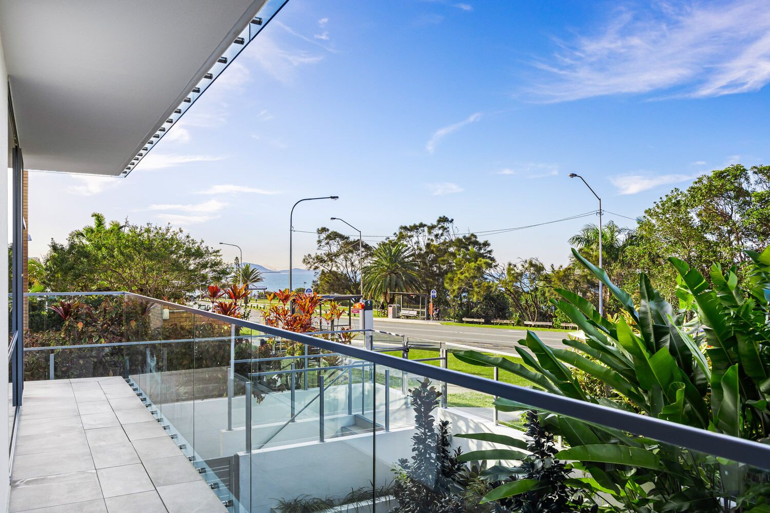 Un bâtiment moderne doté d’un balcon en verre donnant sur une route et des espaces verts.