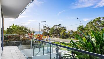 Un bâtiment moderne doté d’un balcon en verre donnant sur une route et des espaces verts.