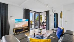 Una sala de estar moderna con televisor, sofás de cuero y vista a una playa a través de la puerta de vidrio.