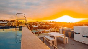 Zona de piscina en la azotea con vistas a un atardecer sobre un barrio residencial.